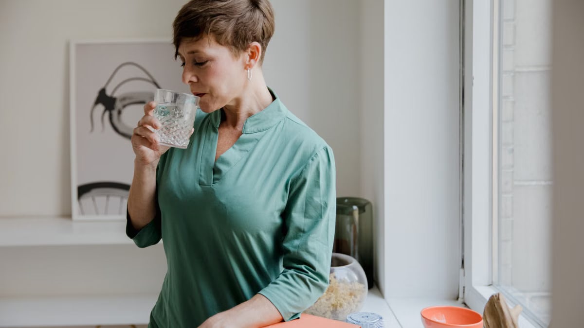 Adult woman savoring water by a window, creating a serene indoor ambiance.